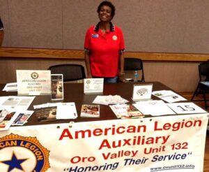 American Legion Auxiliary 132 member in red shirt behind information table for American Legion Auxiliary Units.