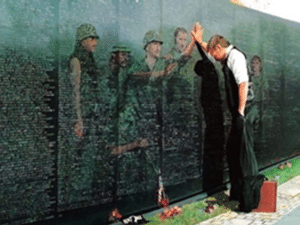 Person touching Vietnam Wall with images of military members reflected in wall.