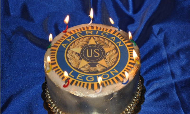 Cake with candles and American Legion logo against blue background.