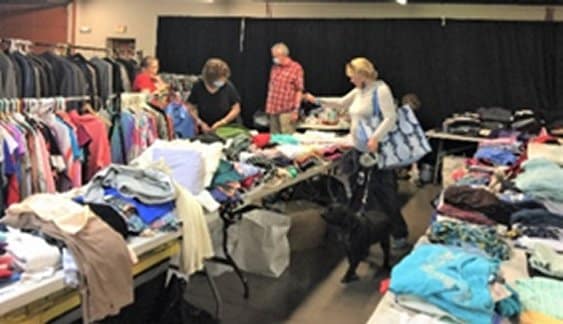 Three volunteers at Stand Down event sorting and organizing donated clothing on tables.