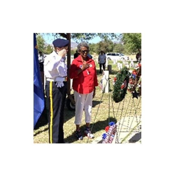 Memorial Day ceremony with Post 132 Honor Guard member saluting wreaths on stand, Auxiliary Unit 132 member saluting with hand over heart.