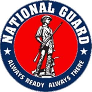 National Guard round emblem with Minuteman statue in the center on a field of red with white lettering in blue field around border of emblem.