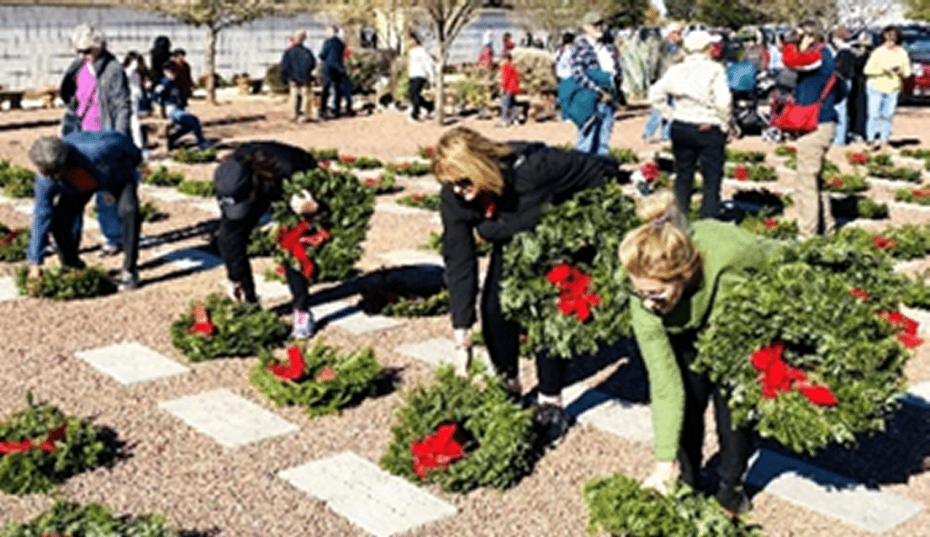 View of men and women placing green wreaths with red ribbons on the headstones of Veterans graves.