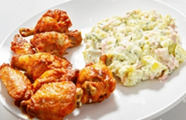 White plate with baked chicken wings and potato salad.